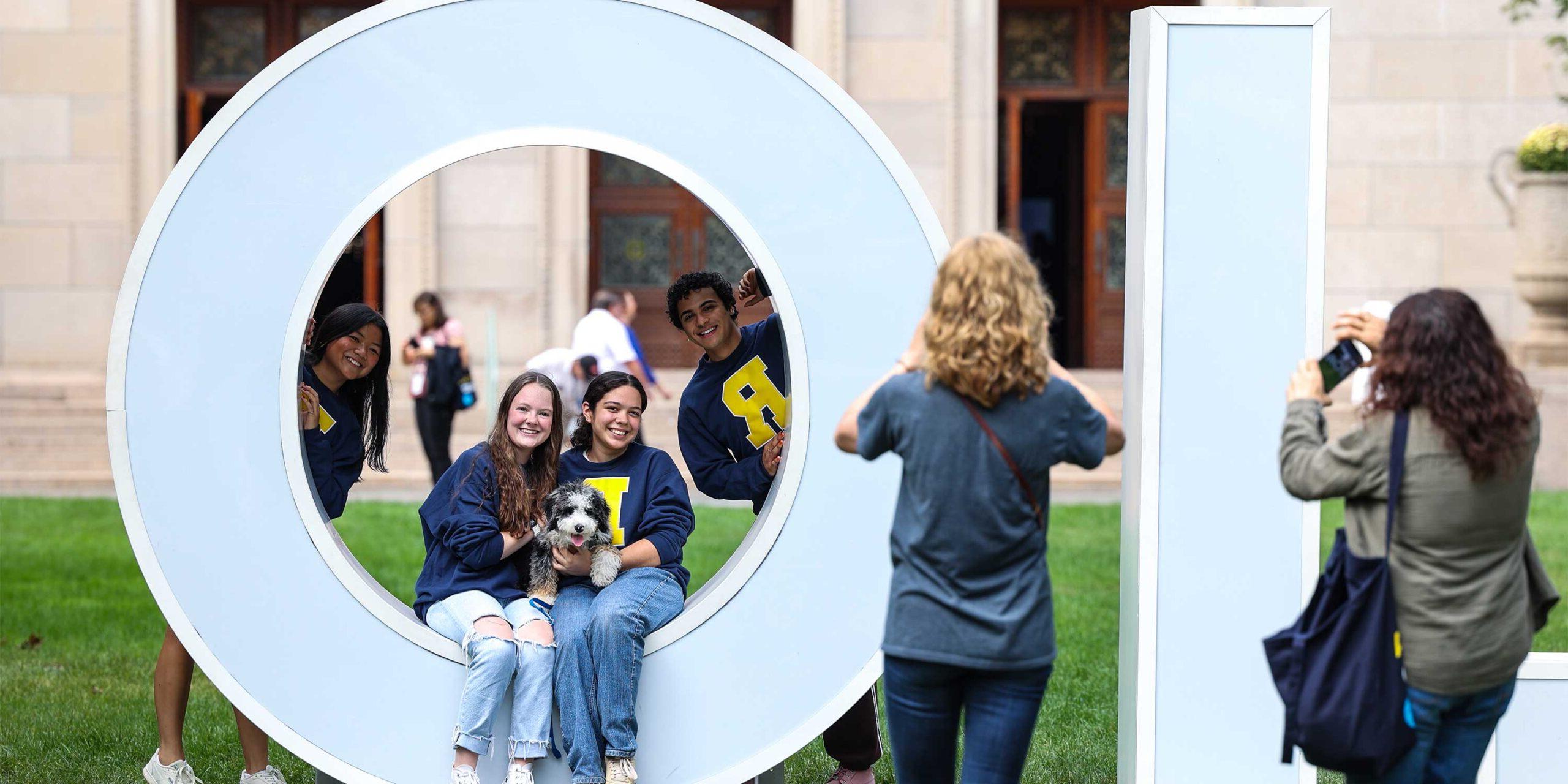 A woman taking a photo of two women sitting in the O of the large white MELIORA letters